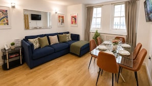 Una sala de estar moderna con un sofá azul, una mesa de comedor preparada para cuatro personas y un televisor de pantalla plana montado en la pared.