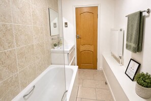 A bathroom with a bathtub, a wooden door, a white sink, a mirror, a towel rack, and a radiator.