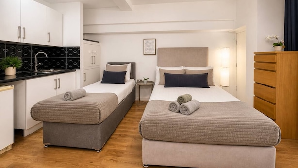 Habitación de hotel con dos camas, kitchenette y una mesita de noche.