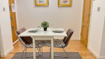 A dining area with a white table, two chairs, a small potted plant, and two framed pictures on the wall.