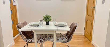Un comedor con una mesa blanca, dos sillas, una pequeña planta en maceta y dos cuadros en la pared.