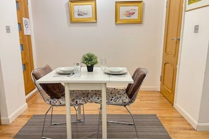 A dining area with a white table, two chairs, a small potted plant, and two framed pictures on the wall.