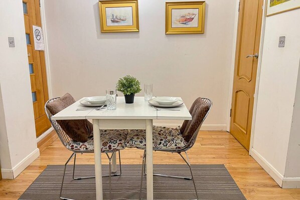 A dining area with a white table, two chairs, a small potted plant, and two framed pictures on the wall.