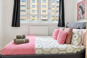 A bedroom with a bed, pillows, a radiator, and a window with curtains. - Bright 3 Bed flat with Balcony near Finsbury Park (Harringay)