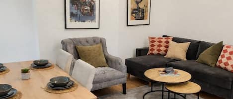 A living room with a sofa, armchair, coffee table, and a dining table with bowls.