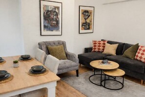 A living room with a sofa, armchair, coffee table, and a dining table with bowls.