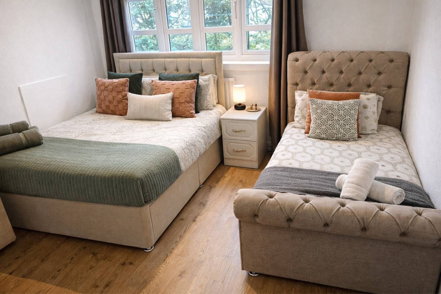 Quarto com duas camas, uma mesa de cabeceira e uma janela.
