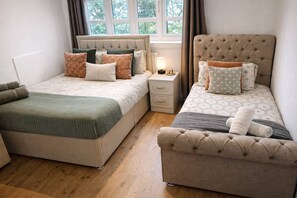 A bedroom with two beds, a bedside table, and a window.