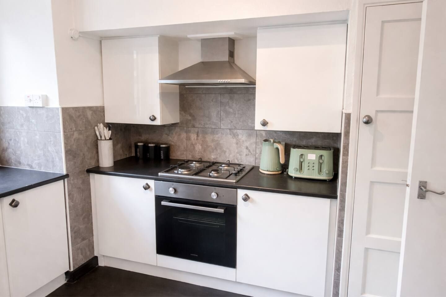 A compact kitchen with white cabinets, a black oven, a gas stove, and a green kettle.