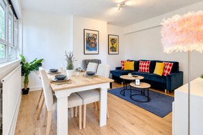 Ein modernes Wohnzimmer mit Essbereich, einer Couch mit gemusterten Kissen und Kunstwerken an den Wänden.
