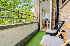 A balcony with a metal railing, a small patch of artificial grass, and two wooden chairs with cushions. - Bright 3 Bed flat with Balcony near Finsbury Park (Harringay)
