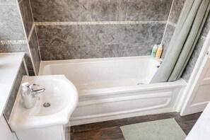 A bathroom with a white bathtub, a sink with a soap dispenser, and a shower curtain.
