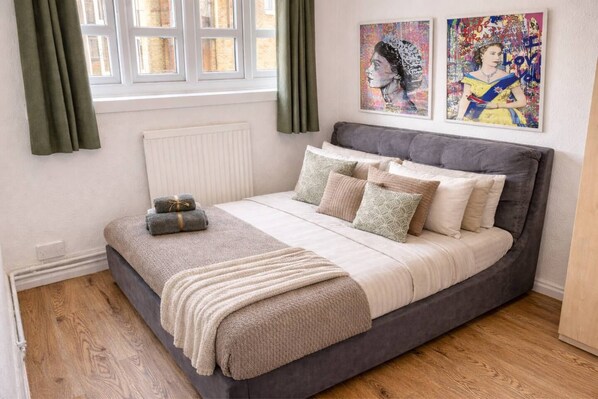 A bedroom with a grey bed, a radiator, a window with curtains, and two wall art pieces.