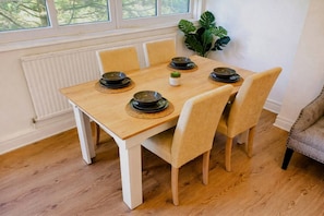 A dining table with four chairs, a plant, and a window with a view of trees.