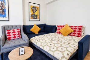 Ein Zimmer mit einer Couch, einem Sessel und einem kleinen Tisch. An der Wand hängt ein gerahmtes Bild und auf dem Tisch befindet sich ein QR-Code.