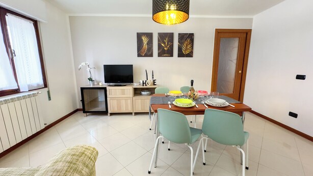 Een eetgedeelte met een tafel voor vier personen, een televisie op een dressoir en een decoratieve wandversiering boven de tafel.