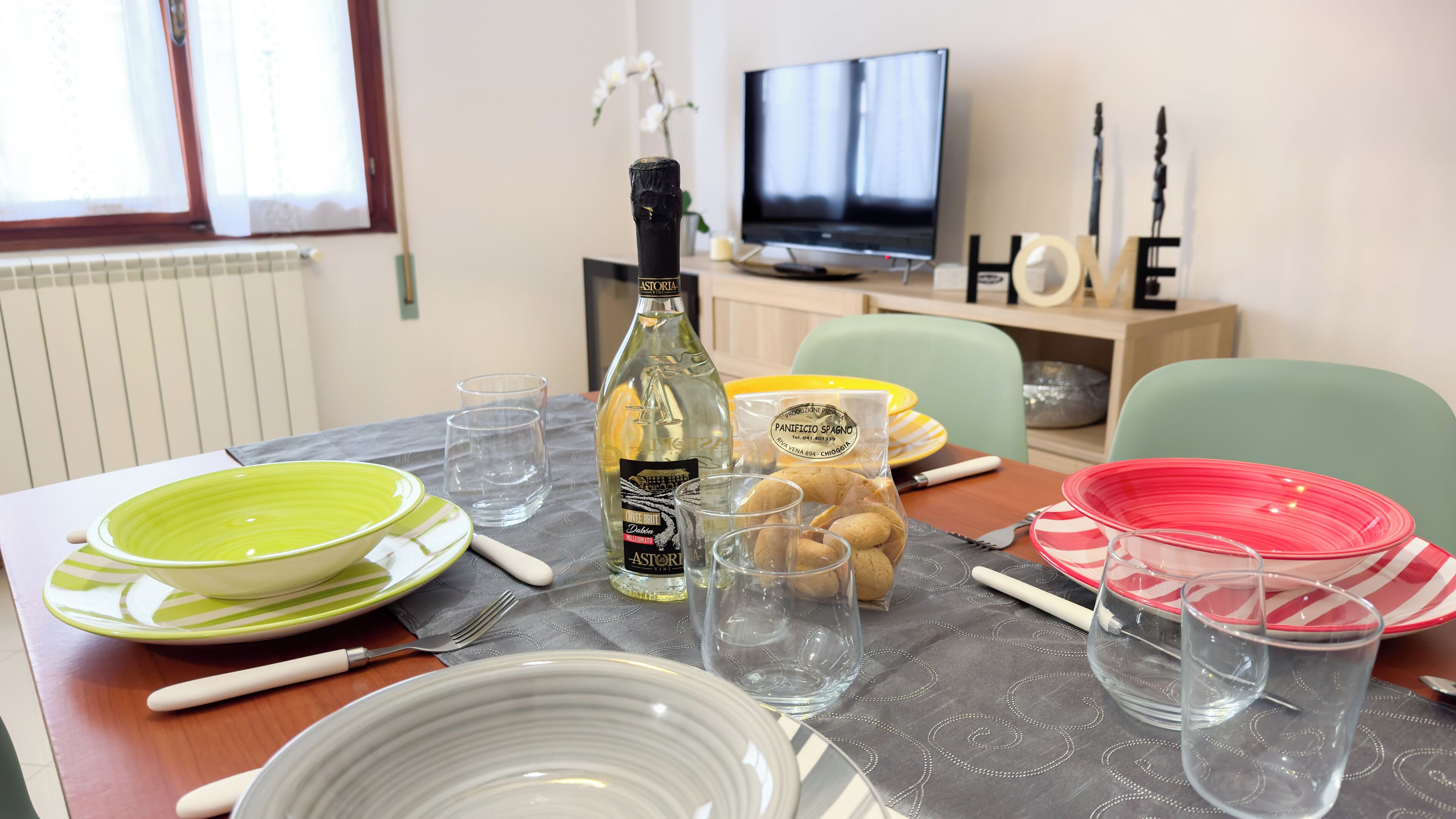Una mesa de comedor dispuesta con platos, vasos, una botella y un bol.