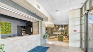 A modern reception area with a stone counter, a blue carpet, and a seating area with sofas and a coffee table. - Uptown Inn by Vantaggio - Limited Service Apart-Hotel (San Diego)