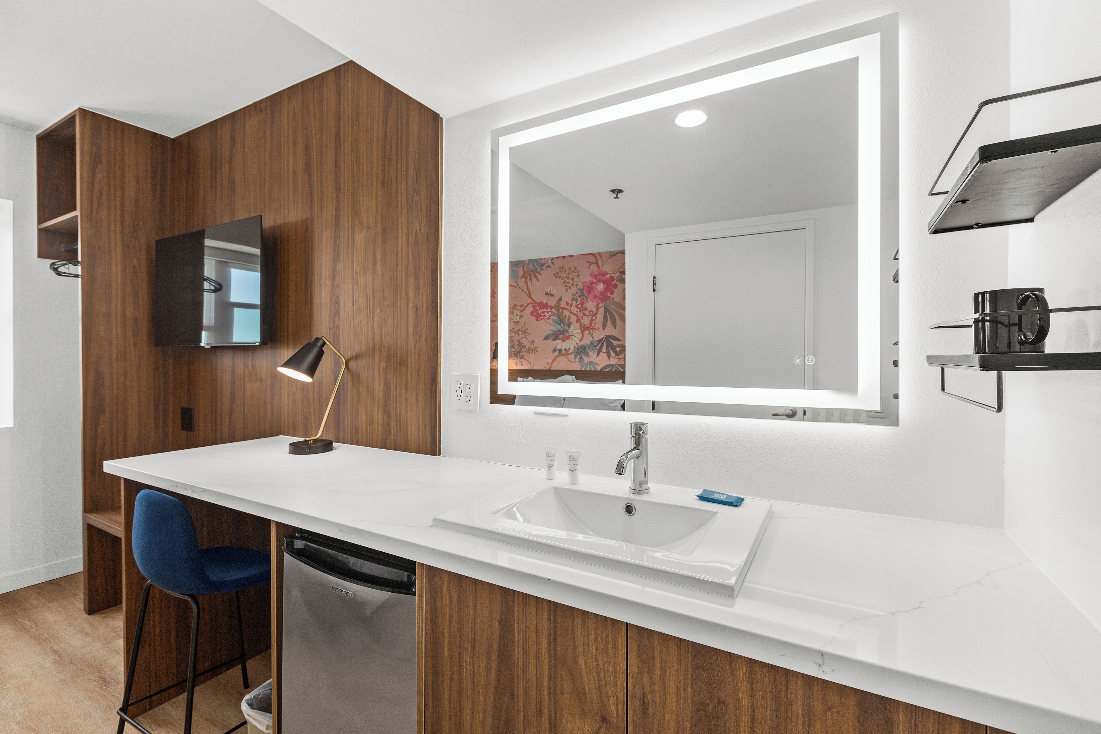 Een moderne badkamer met een wit wastafelmeubel, houten kastjes, een grote spiegel en een blauwe stoel.