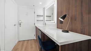 A modern bathroom with a white vanity, a mirror, a black desk lamp, and a blue chair. - Uptown Inn by Vantaggio - Limited Service Apart-Hotel (San Diego)