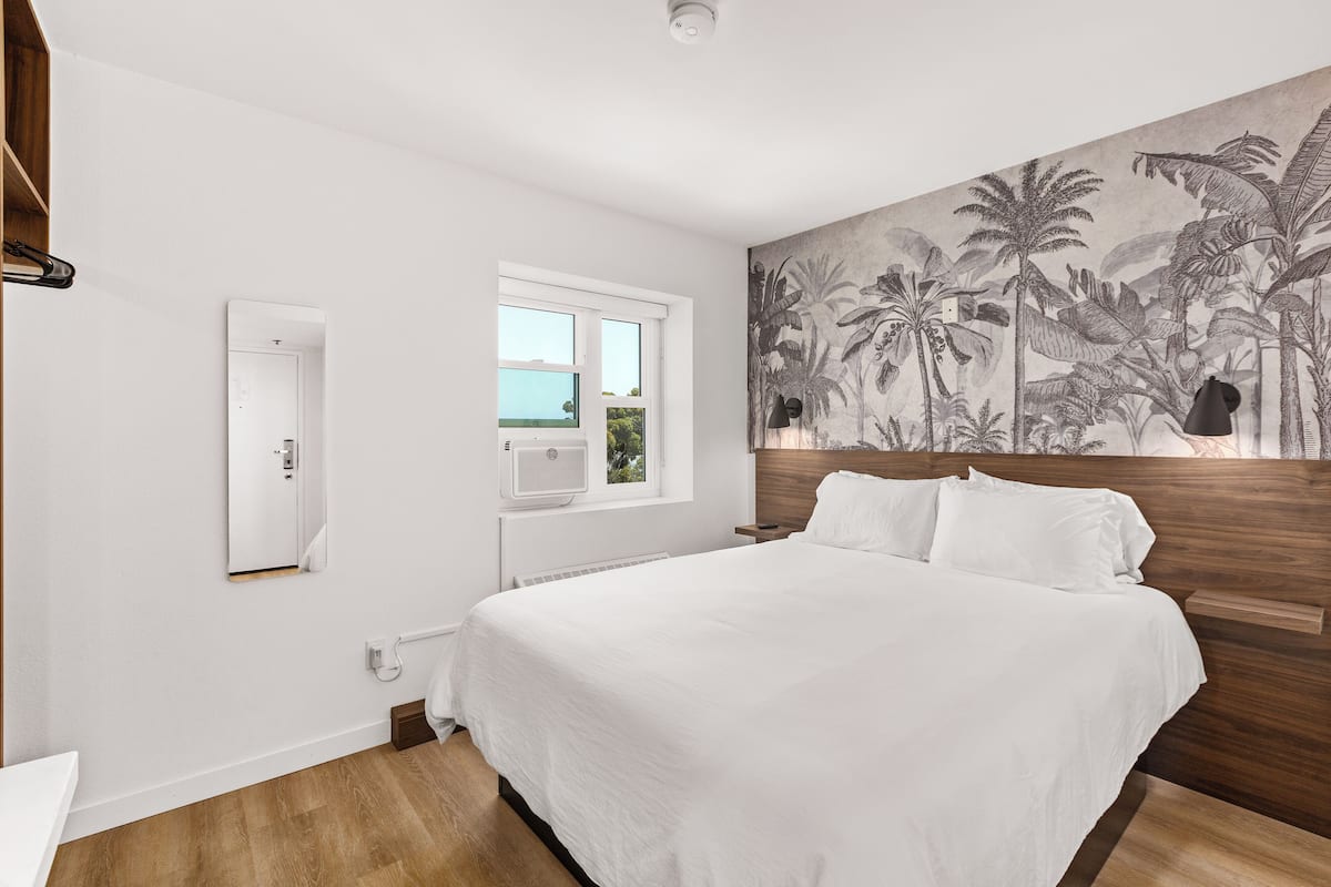 Ein Schlafzimmer mit einem großen Bett, einem Fenster, einer Wandklimaanlage und einem tropischen Wandbild.