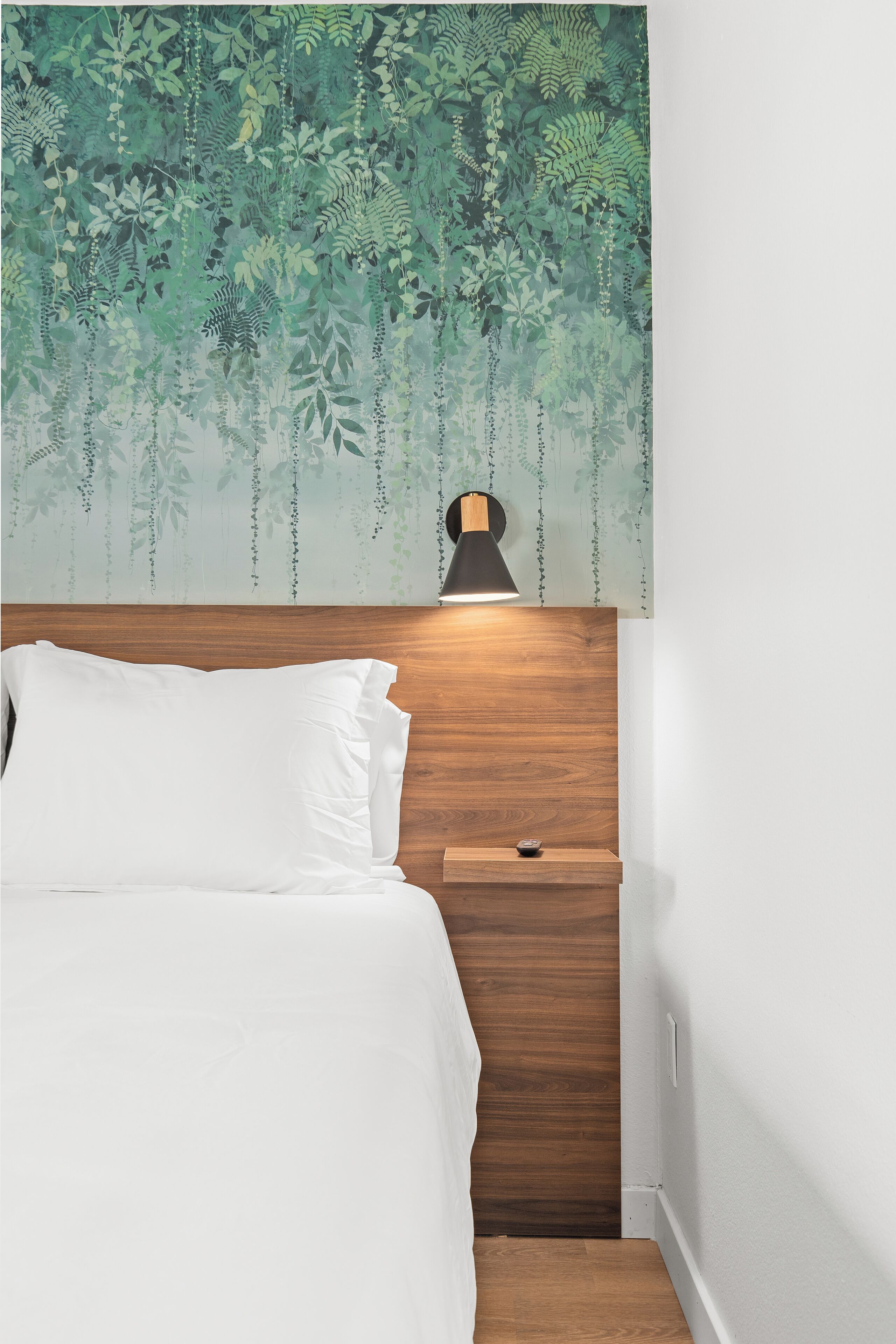 A bedroom with a wooden headboard, a bedside table, and a wall-mounted lamp.