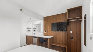 A modern bedroom with a large bed, a wooden wardrobe, a desk with a mirror, and a TV mounted on the wall. - Uptown Inn by Vantaggio - Limited Service Apart-Hotel (San Diego)