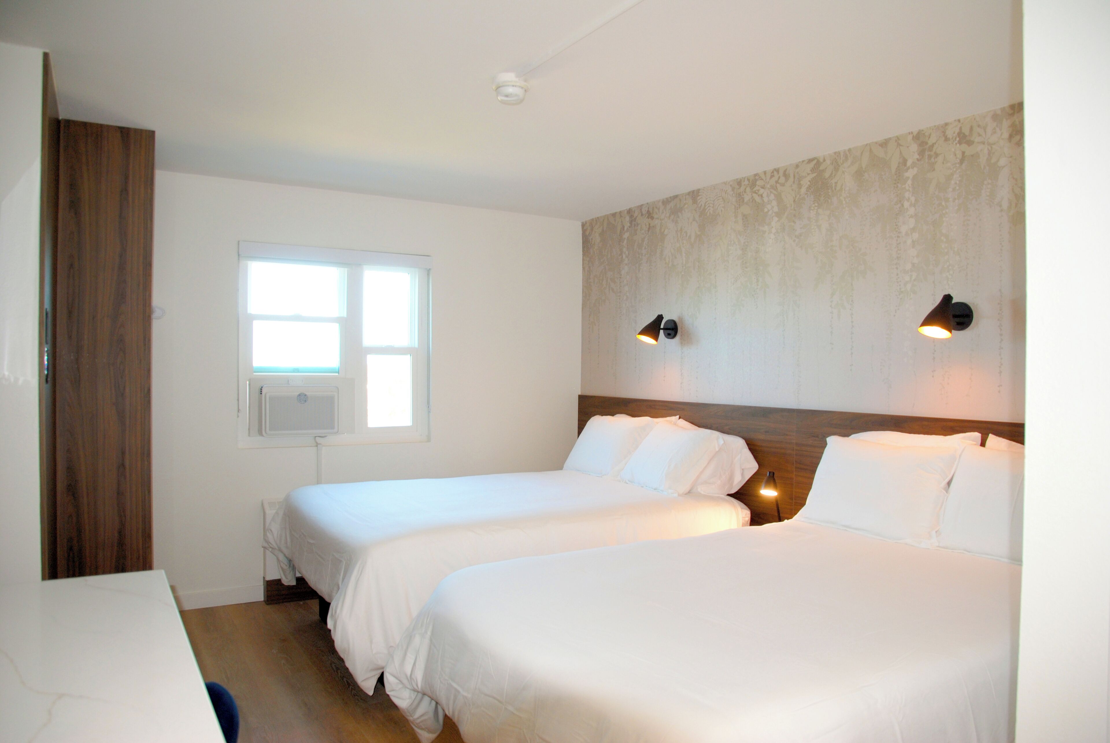 Ett hotellrum med två sängar, en garderob i trä, ett fönster och väggmonterade lampor.