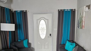 A modern living room with two grey sofas, a ceiling fan, and a door with a decorative glass panel.