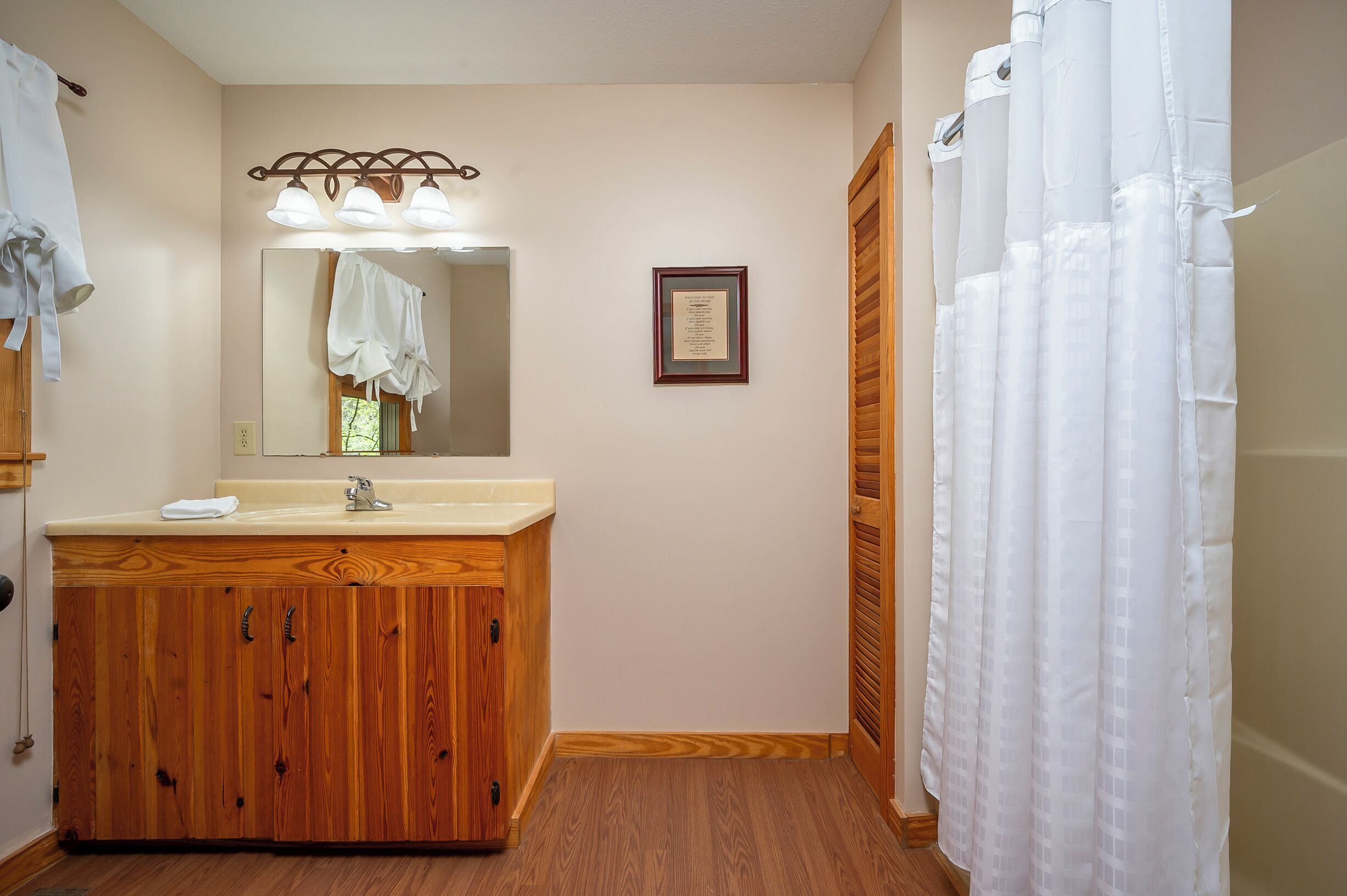 A bathroom with a wooden vanity, a mirror, a framed certificate, and a white shower curtain.