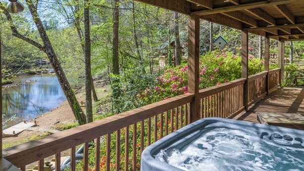 A wooden deck with a hot tub, overlooking a pond and lush greenery.