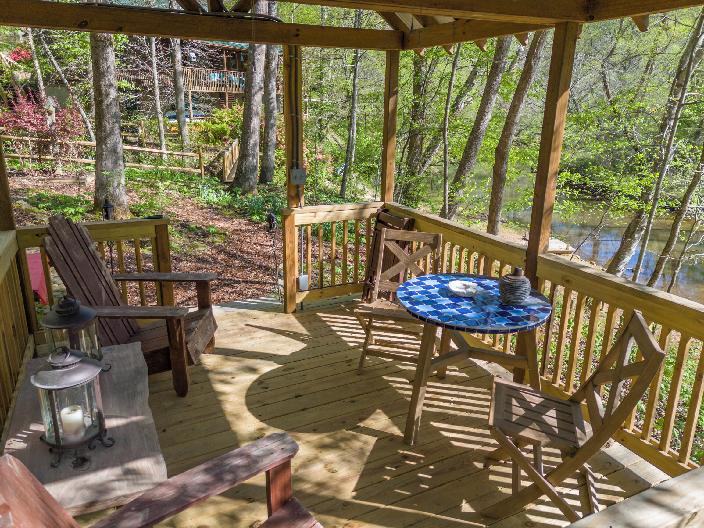 Een houten terras met een tafel en stoelen, omringd door bomen en een waterpartij.