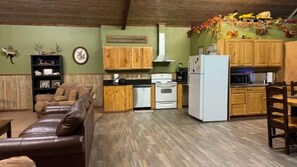 Una sala de estar con sofá, una mesa de comedor con sillas, una cocina con armarios de madera, un refrigerador y una estufa.