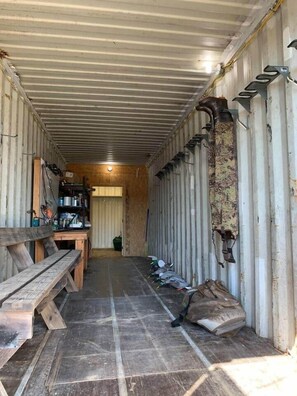 A narrow corridor with a wooden bench on the left, a small table with various items, and a row of boots on the right. - Grandview Acres Bunkhouse (DeWitt)