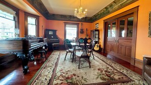 A room with a grand piano, a dining table with chairs, a chandelier, and a large window. - Hubble House Inn (Montesano)