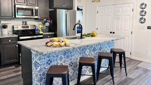 A modern kitchen with dark cabinets, stainless steel appliances, a tiled island with bar stools, and hanging pendant lights. - 2 Primary EnSuites, HOT Tub, Firepit, Hammock, Min to St Augustine, DOG-Friendly (St. Augustine)