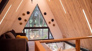 Een gezellige, driehoekige kamer met een houten plafond, een groot raam en een houten bankje.