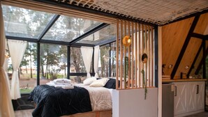 Een slaapkamer met een bed, een klein bureau en een raam met uitzicht op een bos.