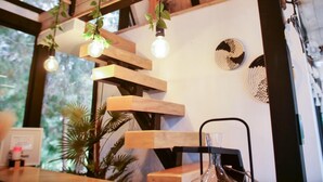 Een houten trap met hangplanten en lichtbollen, een zwarte stoel en decoratieve wandkunst.
