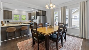 A modern kitchen with a central island, dark wooden chairs, and a chandelier. - Adorable Bungalow, Minutes from Downtown Durham (Durham)