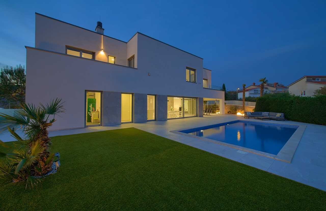 Een modern huis met twee verdiepingen, een zwembad, een verzorgd gazon en een terras.