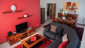 A living room with a red accent wall, a grey sofa, a wooden coffee table, a TV, and a dining area with a wooden table and chairs.
