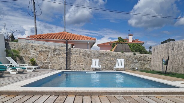 A wooden deck leading to a swimming pool with white lounge chairs and a hammock.