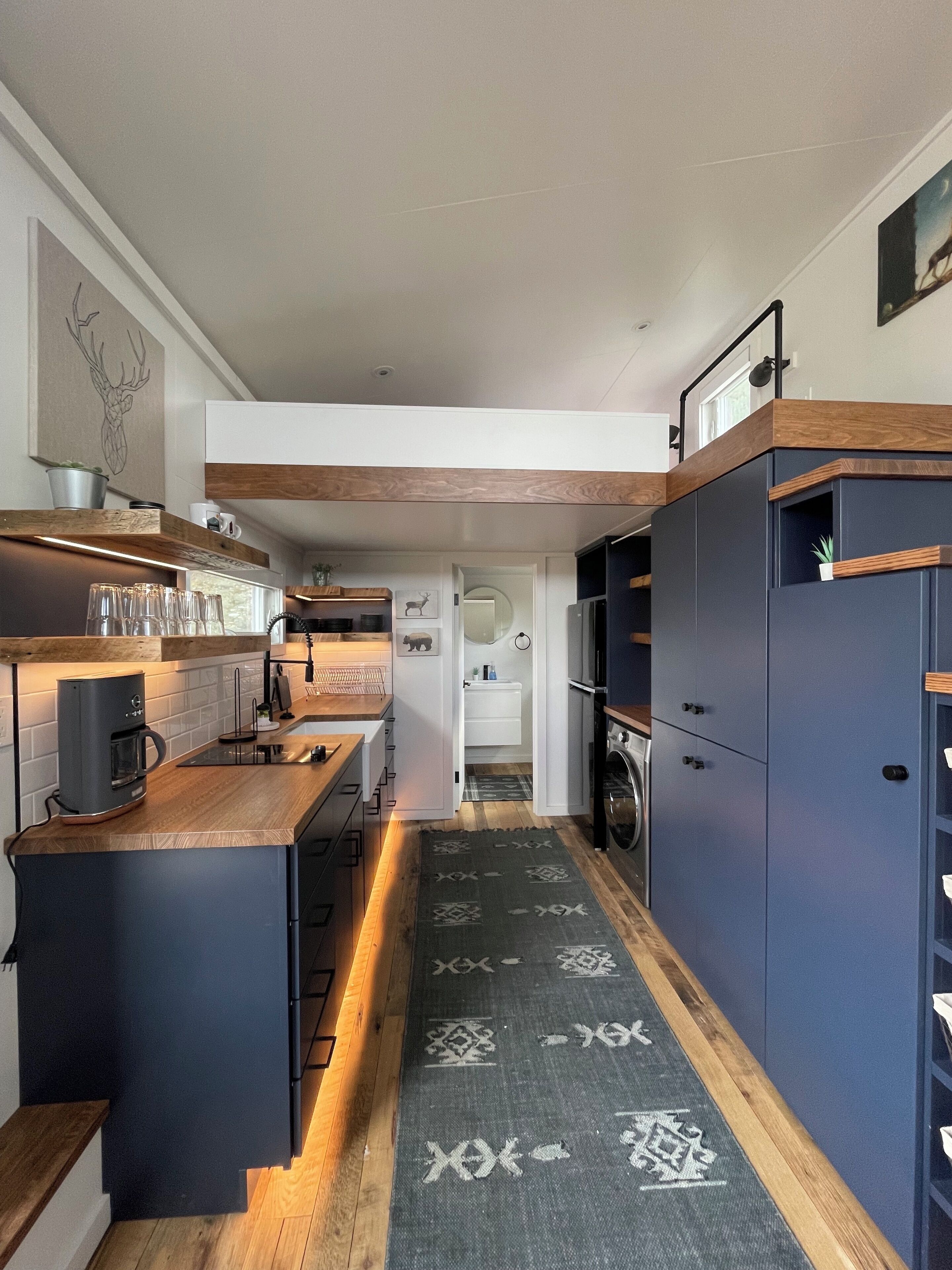 Una cocina moderna con encimeras de madera, horno empotrado y una alfombra estampada que conduce a un baño.