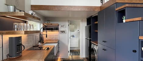 Una cocina moderna con encimeras de madera, horno empotrado y una alfombra estampada que conduce a un baño.