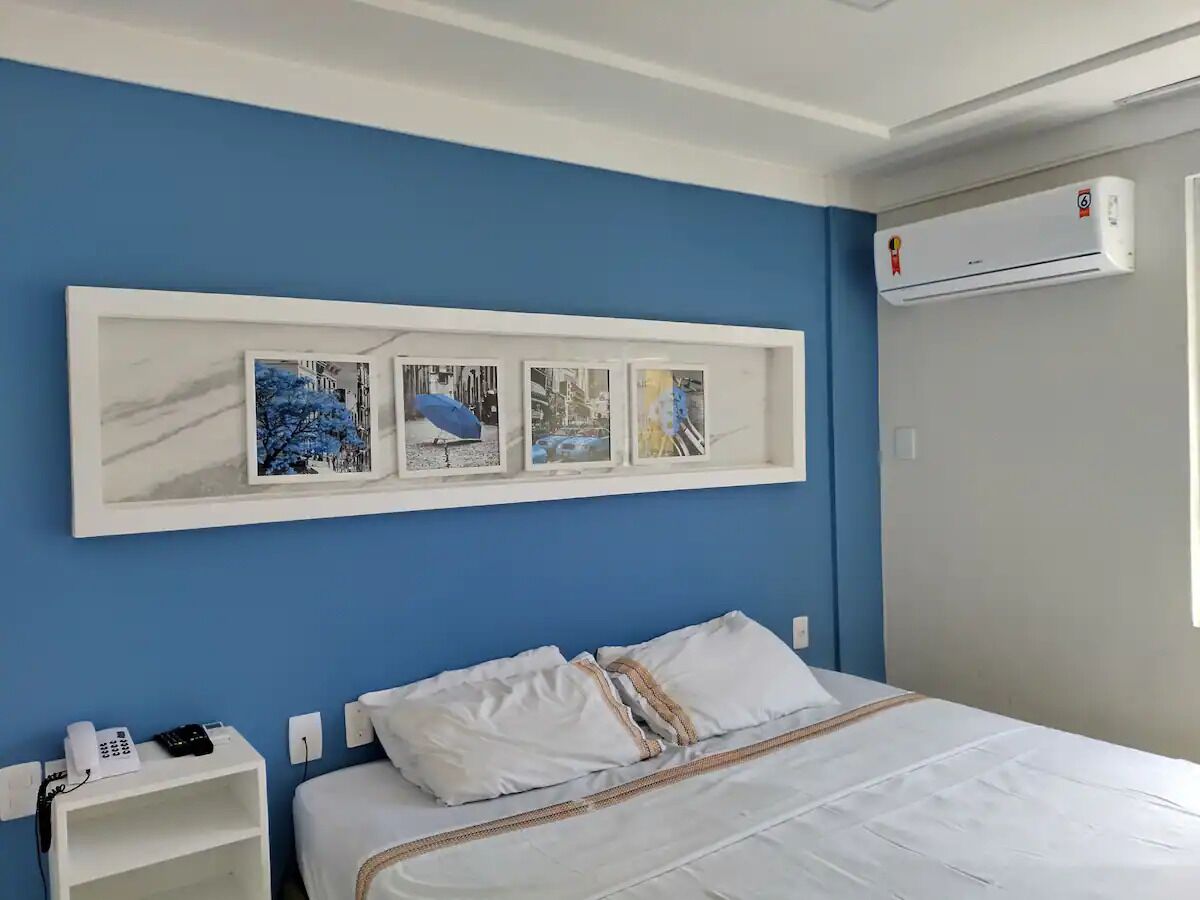Quarto de hotel com cama, mesa de cabeceira com telefone e ar-condicionado fixado na parede.