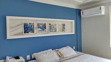 Quarto de hotel com cama, mesa de cabeceira com telefone e ar-condicionado fixado na parede.