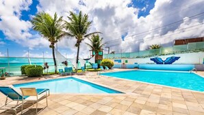 A swimming pool with lounge chairs, palm trees, and a view of the ocean. - Flat Ponta Negra Beach Natal (Natal)