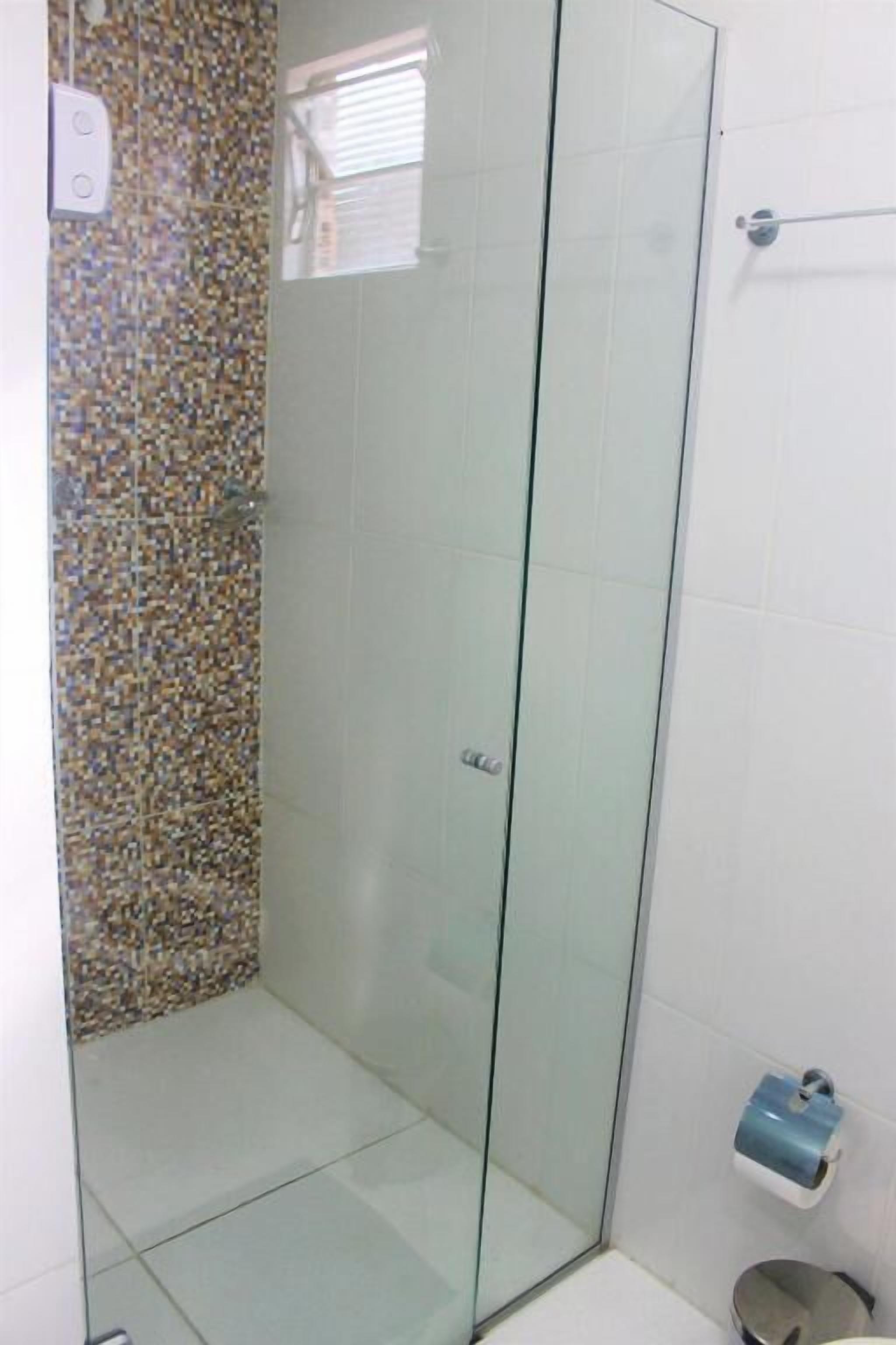 A glass-enclosed shower area with tiled walls and a small shelf with toiletries.