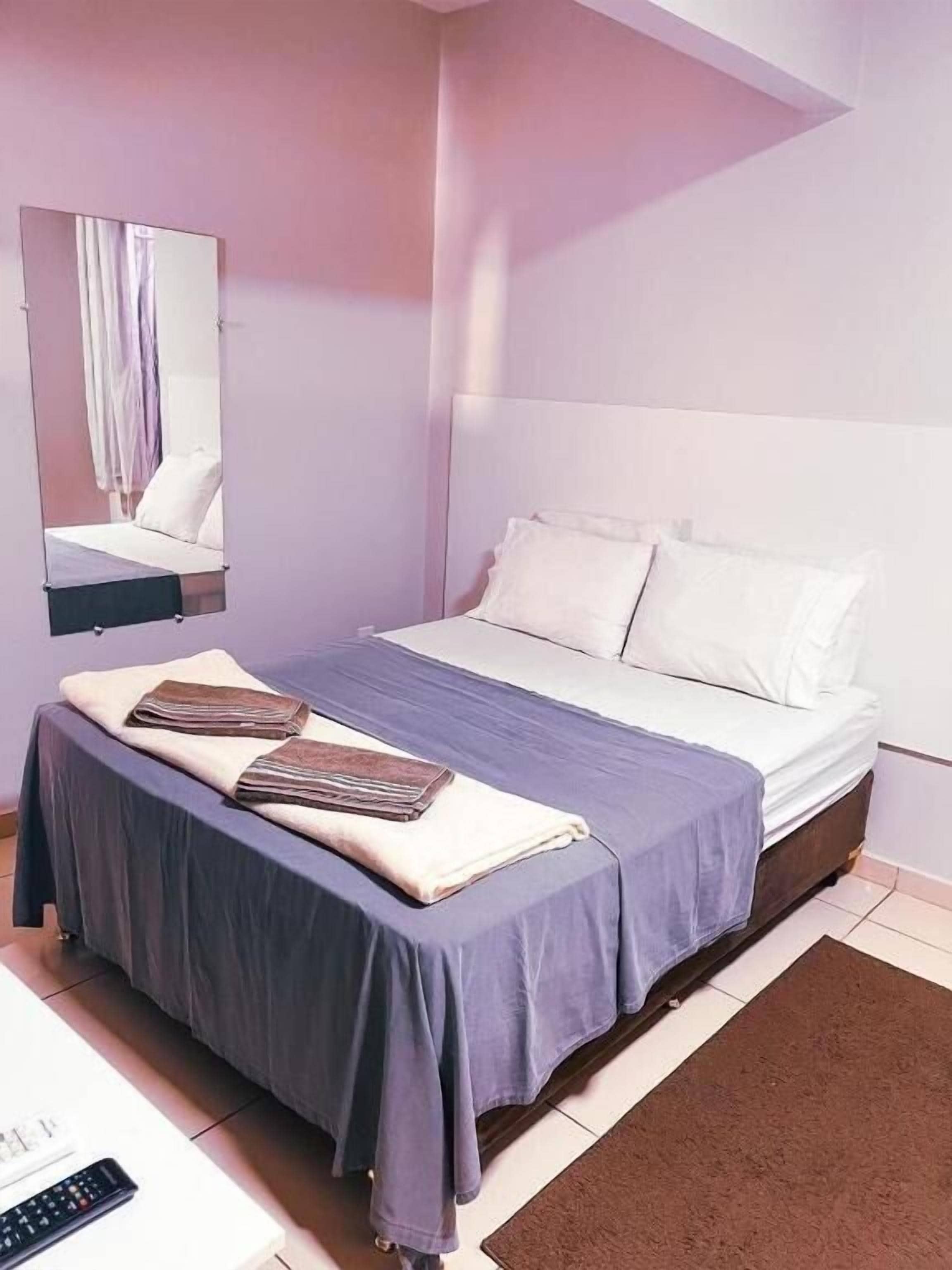 A bedroom with a bed, a nightstand, a remote control, and a brown rug.